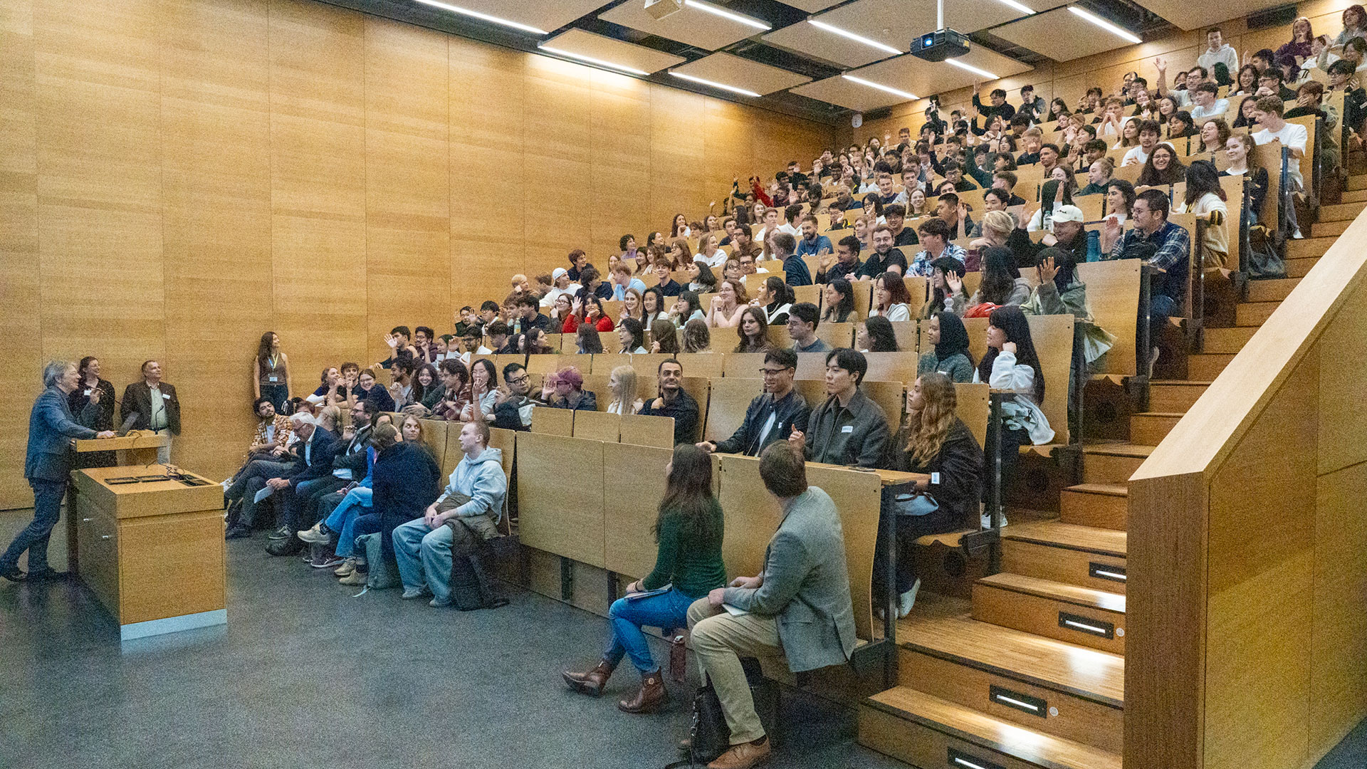 A man at a lecturn and a lecture hall with 200 freshers.