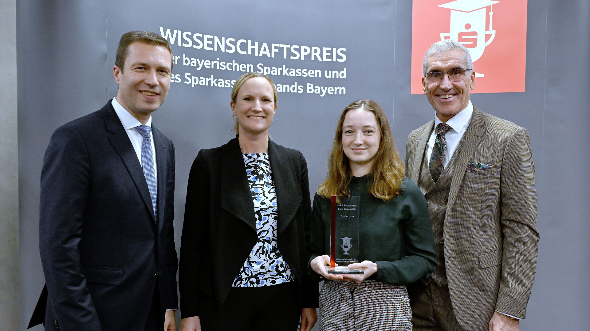 Two women and two man standing in a group, one of the women is presenting a glass trophy.