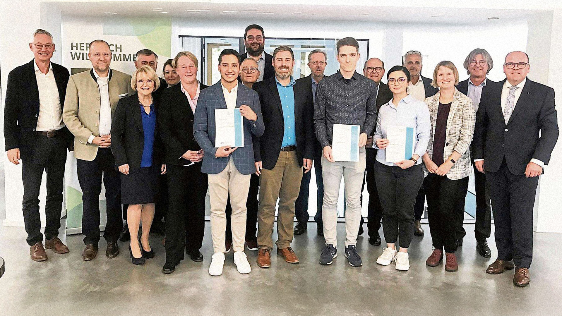 Eine Gruppe von 18 Personen, drei davon präsentieren ihre Zertifikate.