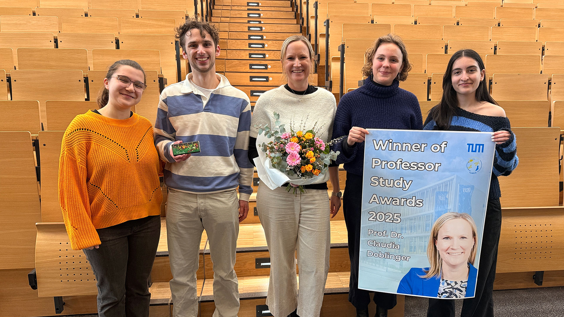 A group of people, one holding a poster and another a bouquet of flowers