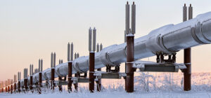 Eine Ölpipeline auf Stelzen in einer schneebedeckten Landschaft beim ersten Sonnenlicht. Die Pipeline läuft diagonal von rechts nach links in den Horizont.