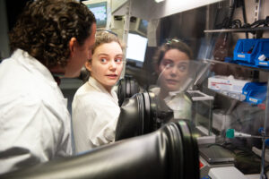 Professor supervising a female doctorate candidate at a glove box in a lab.