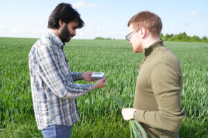 Zwei Männer stehen auf einem Feld und nutzen ein kompaktes Messgerät.
