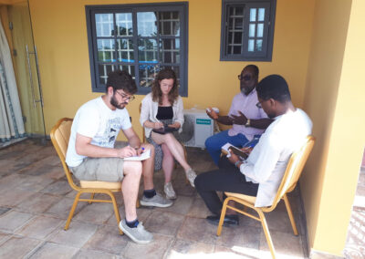 Vier Personen sitzen auf einer Terrasse, sprechen miteinander und machen Notizen.